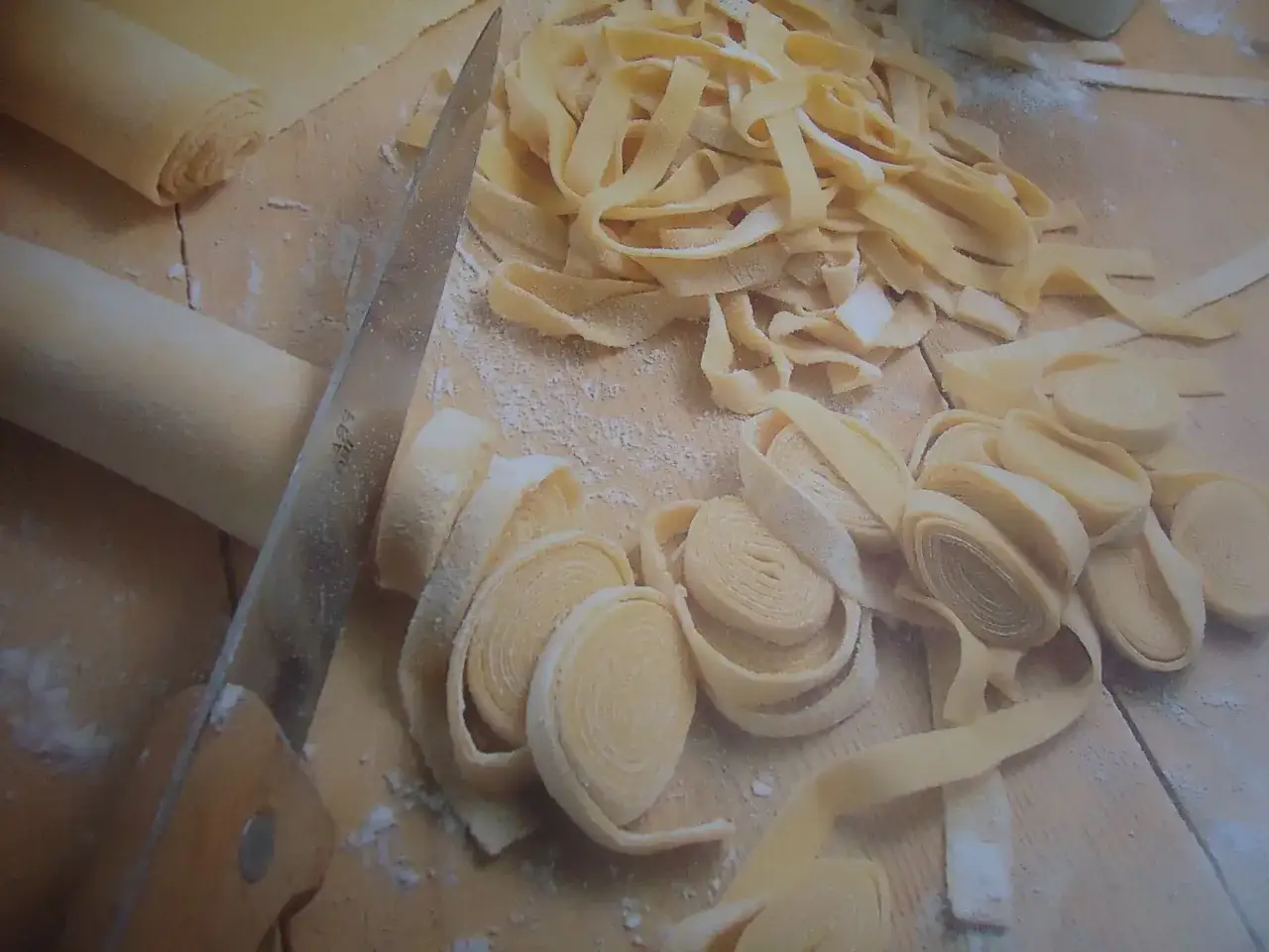 Rotoli di pasta fatta in casa pronti per essere tagliati. Un coltello e un mattarello completano la scena casalinga.