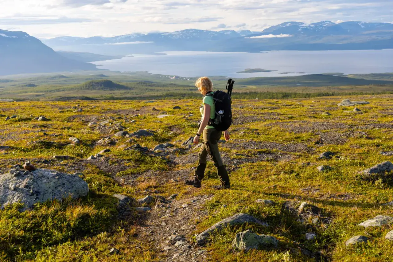 Vandrare med ryggsäck på en stig i Abisko, njuter av utsikten över fjäll och sjö. En perfekt start på en vandring i Abisko 3 dagar.