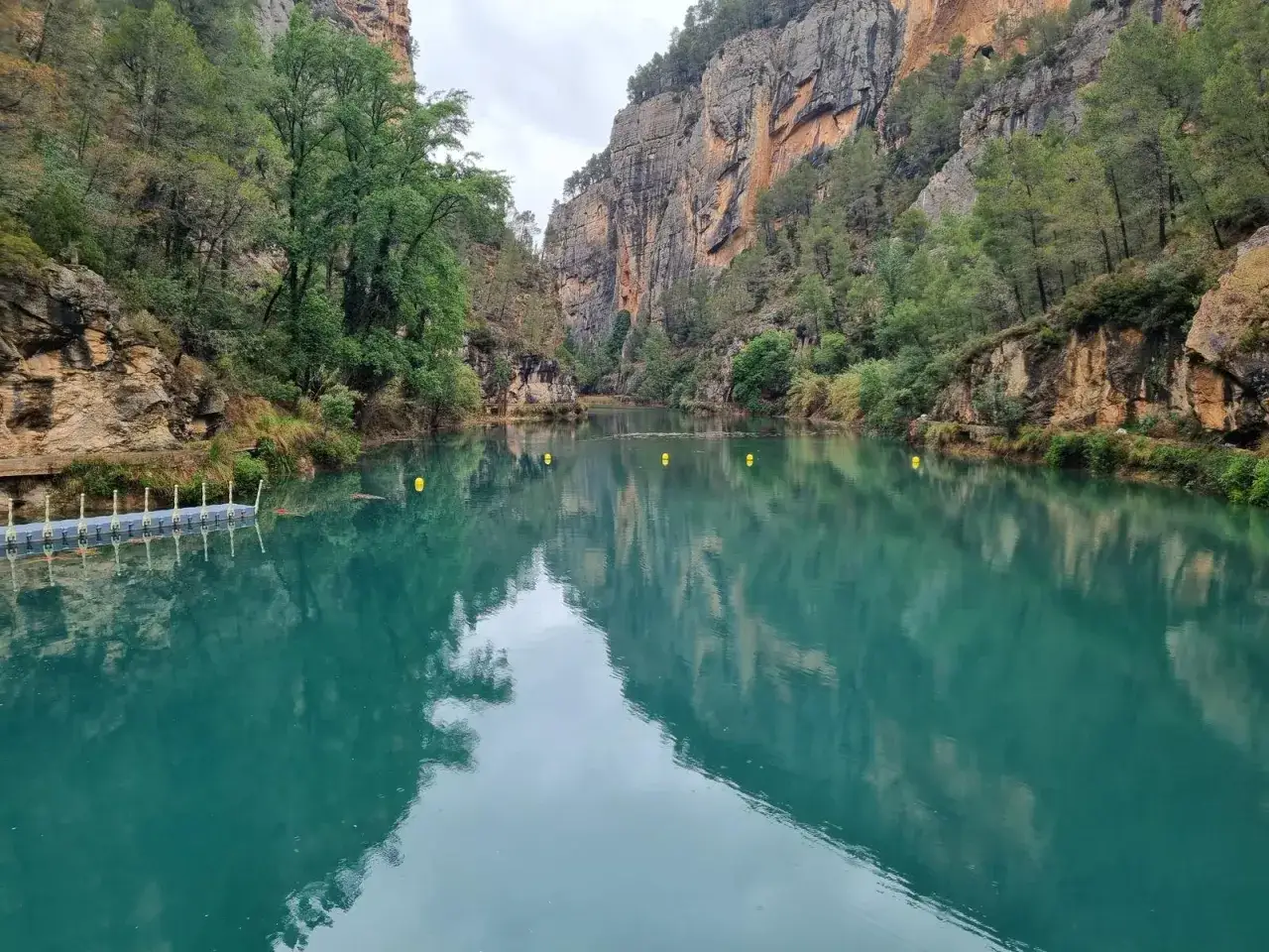 Aguas turquesas en la cueva negra de Montanejos, rodeada de acantilados y vegetación.