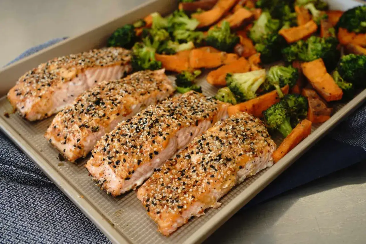 Vier Lachsfilets mit Sesamkruste auf einem Blech mit ger&ouml;stetem Brokkoli und S&uuml;&szlig;kartoffeln. Perfekt f&uuml;r eine pescetarier-Ern&auml;hrung, die Fisch erlaubt.