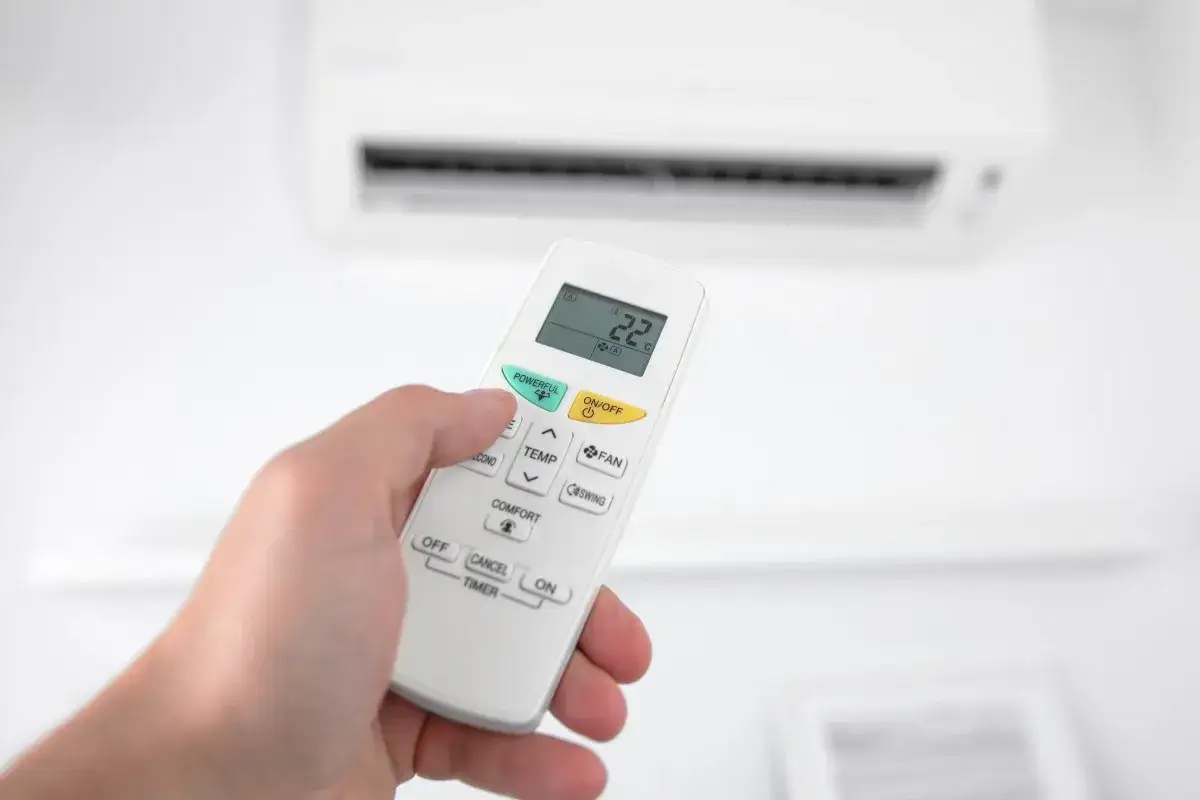 Mano sujetando control remoto para programar aire acondicionado. Pantalla muestra 22°C. Botón