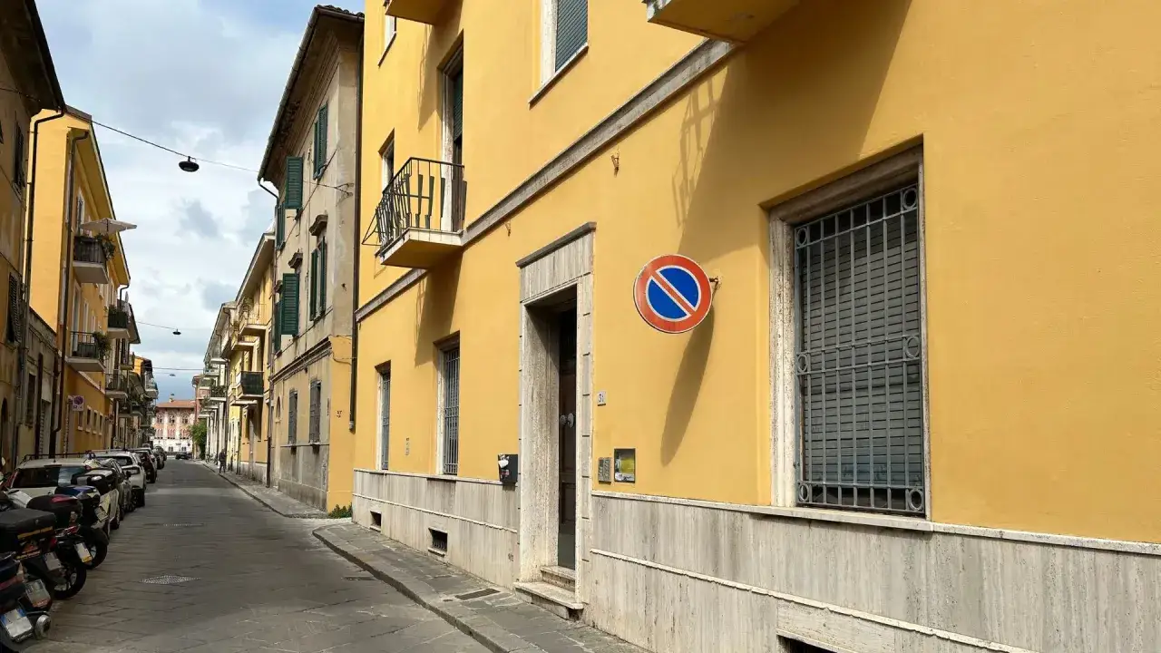 A street in Tuscany with yellow buildings, parked cars, and a no parking sign. Perfect for renting a car and exploring!