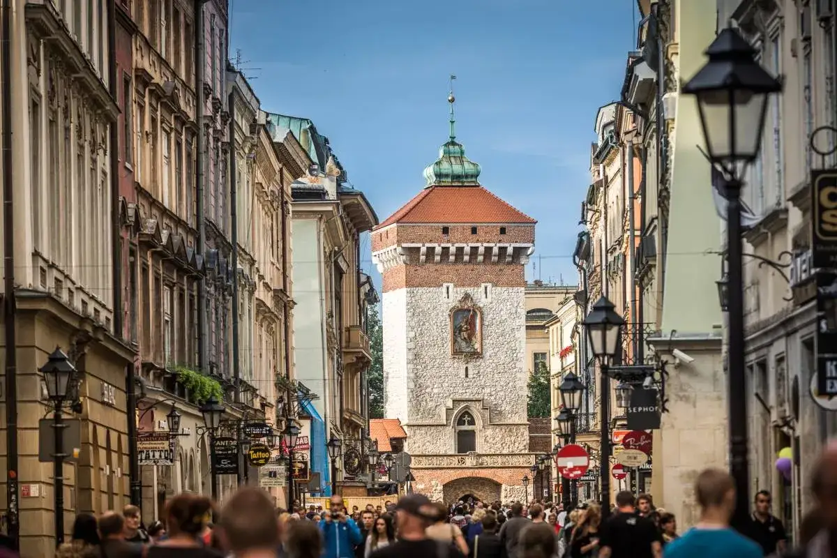 Tłum ludzi idzie ulicą w stronę zabytkowej **Bramy Floriańskiej** z charakterystyczną wieżą i czerwonym dachem.