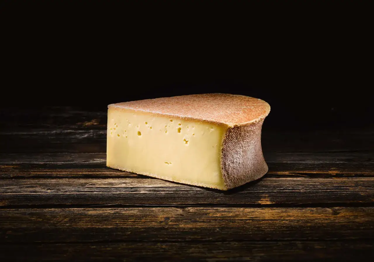 Un morceau de fromage Berthoud, parfait pour une recette savoureuse, posé sur un fond de bois sombre.