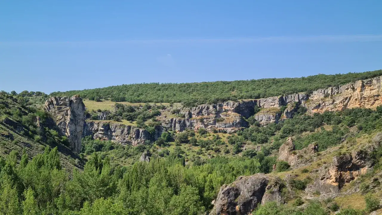 Majestuosas rocas y vegetaci&oacute;n exuberante en la Alcarria Alta, bajo un cielo azul despejado.