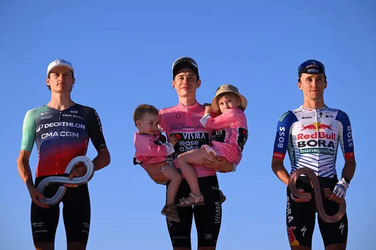 Cyclists on a podium with children. The central figure, possibly Trine Vingegaard, holds two young children.