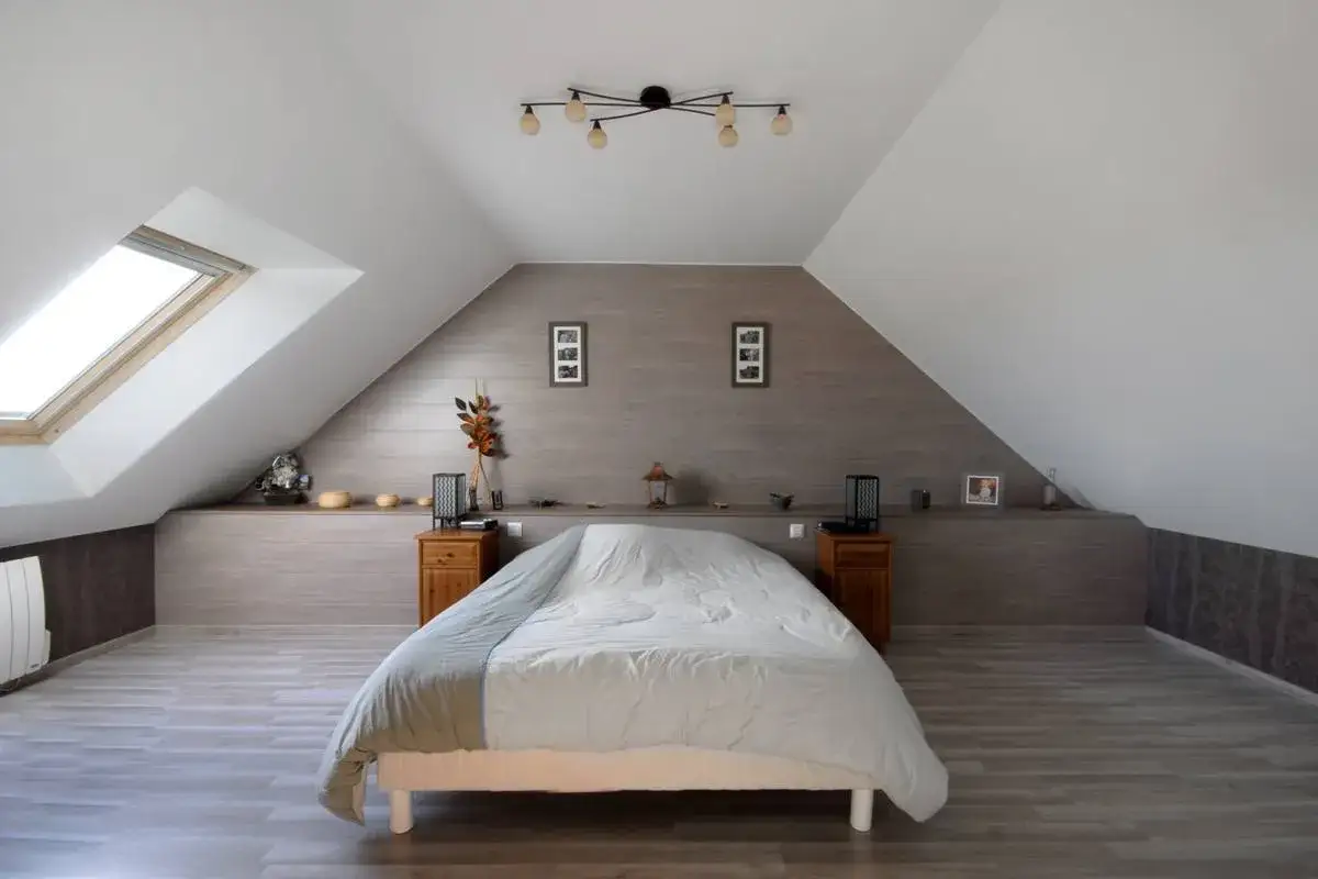 Chambre sous comble avec lit douillet, velux et décoration murale en bois.