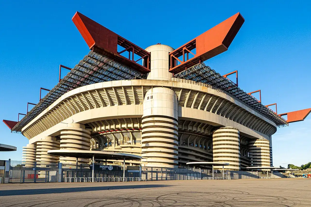 Stadion San Siro, dom dla wielkiego klubu piłkarskiego z Mediolanu, z charakterystycznymi czerwonymi elementami dachu i betonowymi wieżami.
