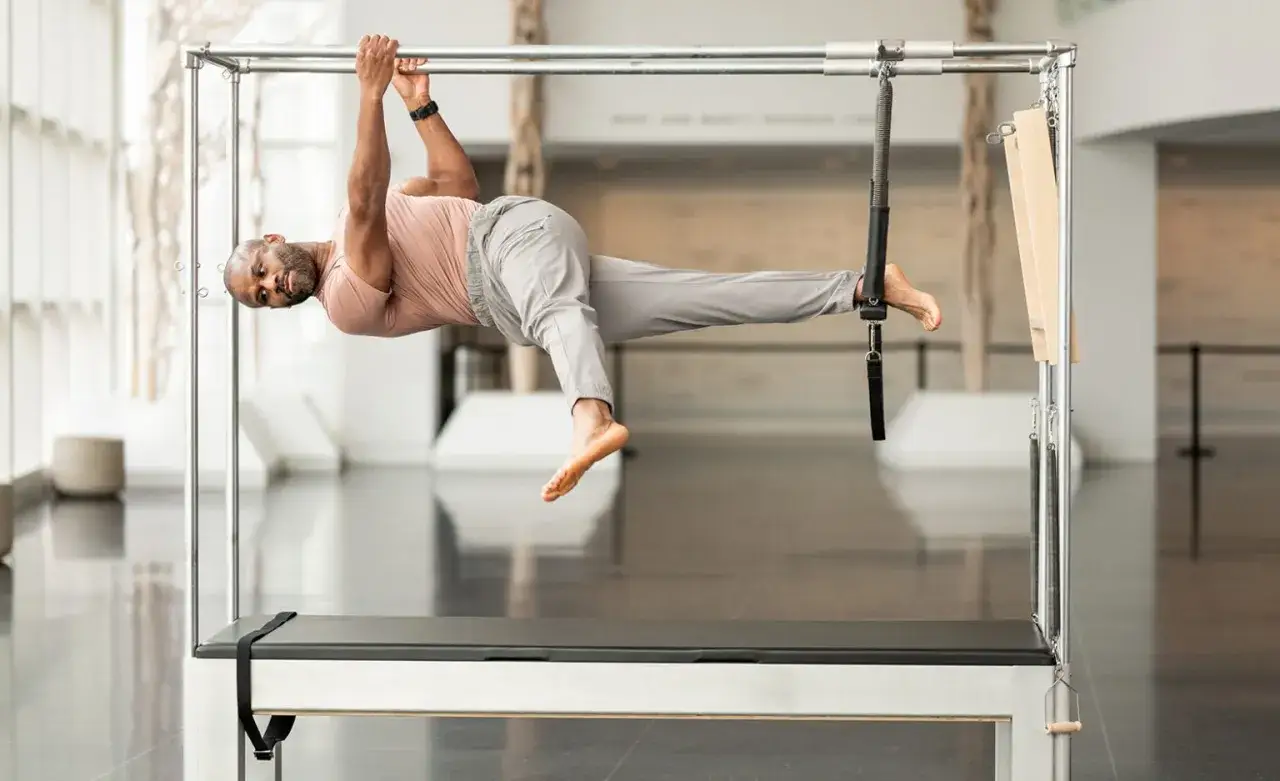 Uomo che esegue un esercizio di pilates sul reformer. Scopri cosa abbinare al pilates per un allenamento completo.