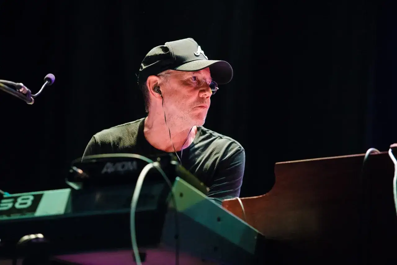 Klawiszowiec w czapce z daszkiem, w słuchawkach, grający na keyboardzie, kontynuuje dire straits legacy.