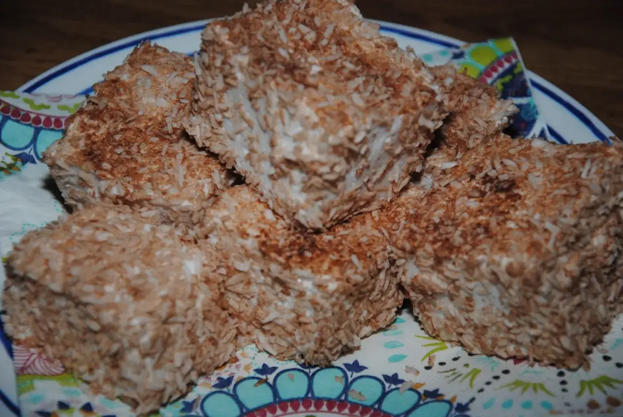En hög med fluffiga kokosbollar, täckta av rostad kokos, ligger på en färgglad servett.