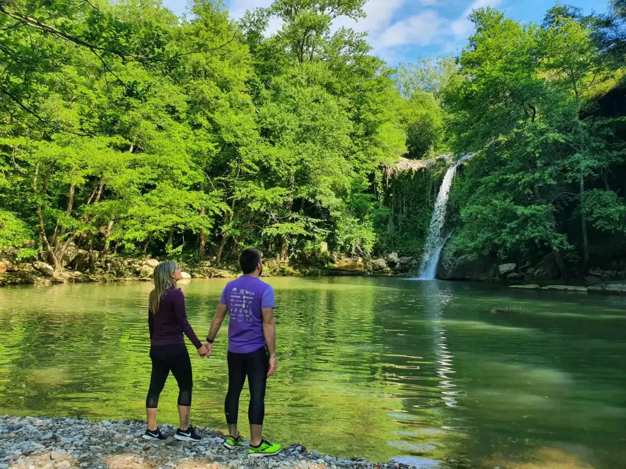 Pareja admirando una cascada en el Vall d'Ora Gorgs. El agua verde esmeralda contrasta con la exuberante vegetaci&oacute;n.