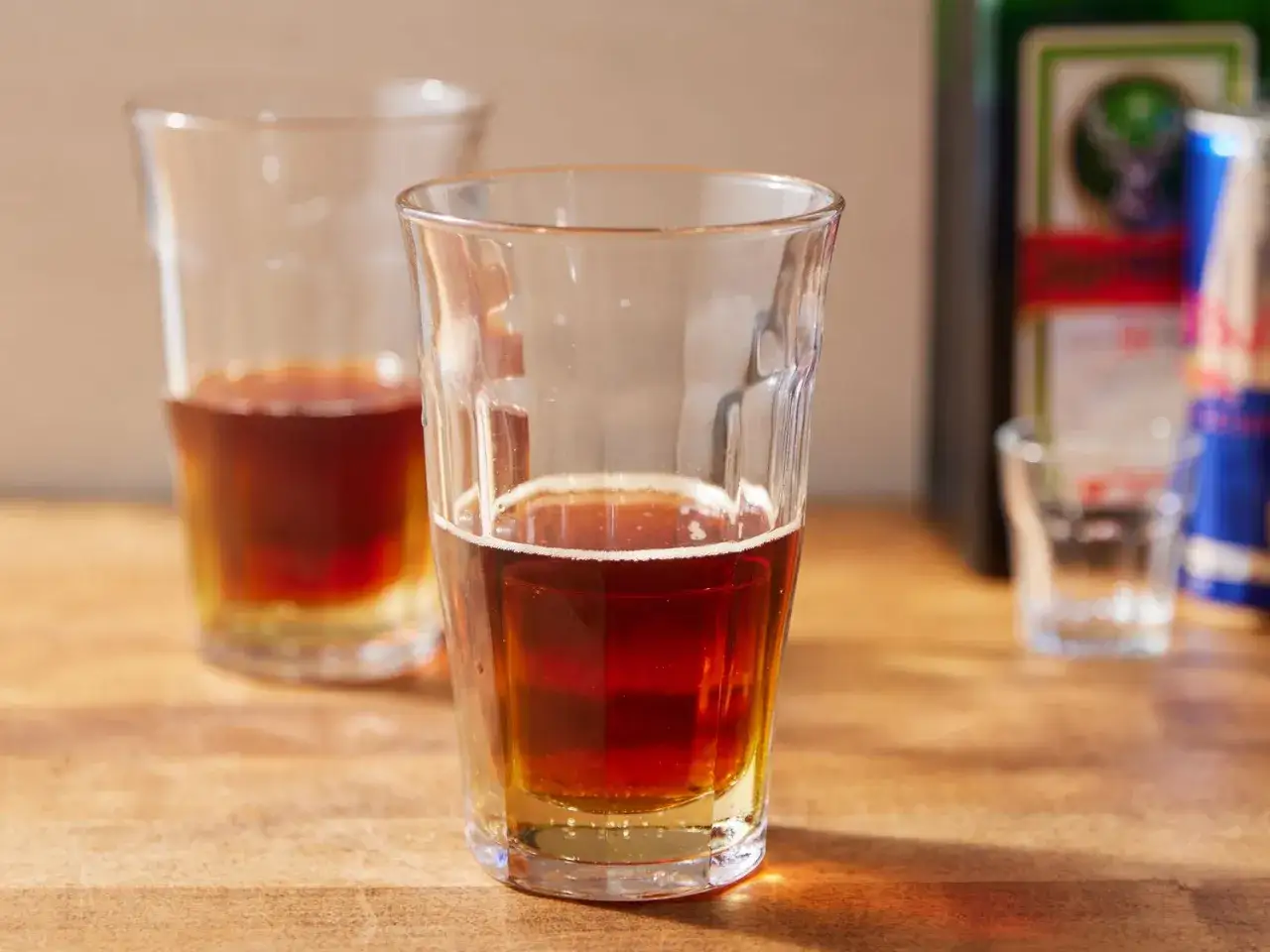 Dwa szklanki z ciemnym napojem, obok butelka Jägermeister i puszka Red Bull. Idealny drink jagermeister red bull na wieczór.