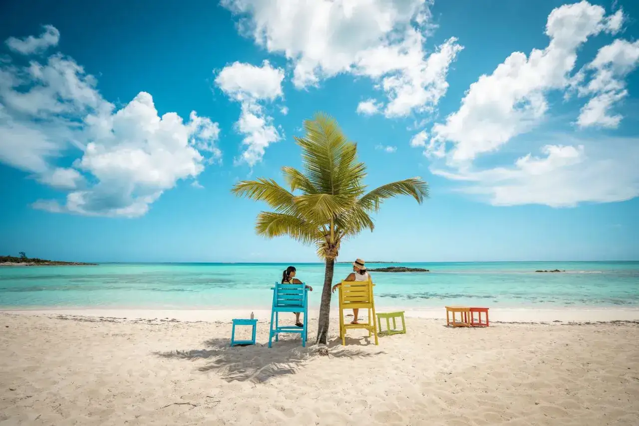 Deux femmes profitent du soleil sur une plage des Bahamas, sous un palmier. Idéal pour savoir que faire aux Bahamas.