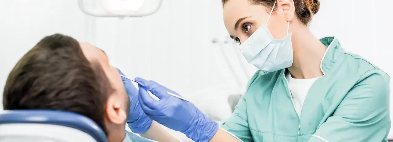Dentystka w masce i rękawiczkach bada ząb pacjenta. Sprawdź leczenie kanałowe NFZ cennik.