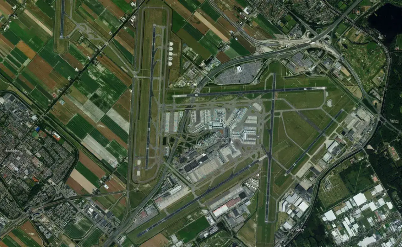 Widok z lotu ptaka na lotnisko Schiphol w Amsterdamie, z pasami startowymi, terminalami i otaczającymi polami uprawnymi.
