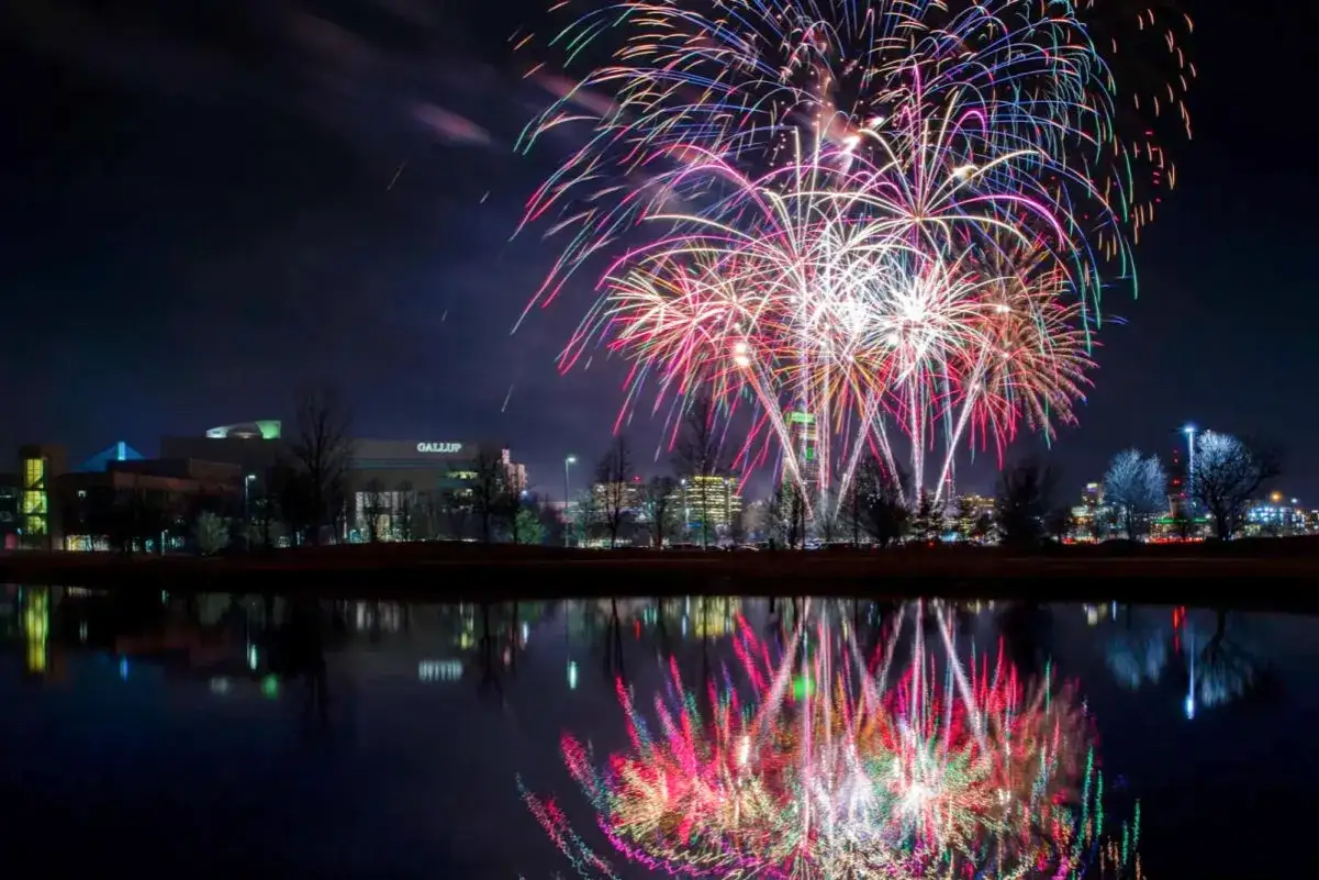 Fuochi d'artificio colorati illuminano il cielo notturno sopra un lago, riflettendo le luci. Celebrazione di Capodanno, o 