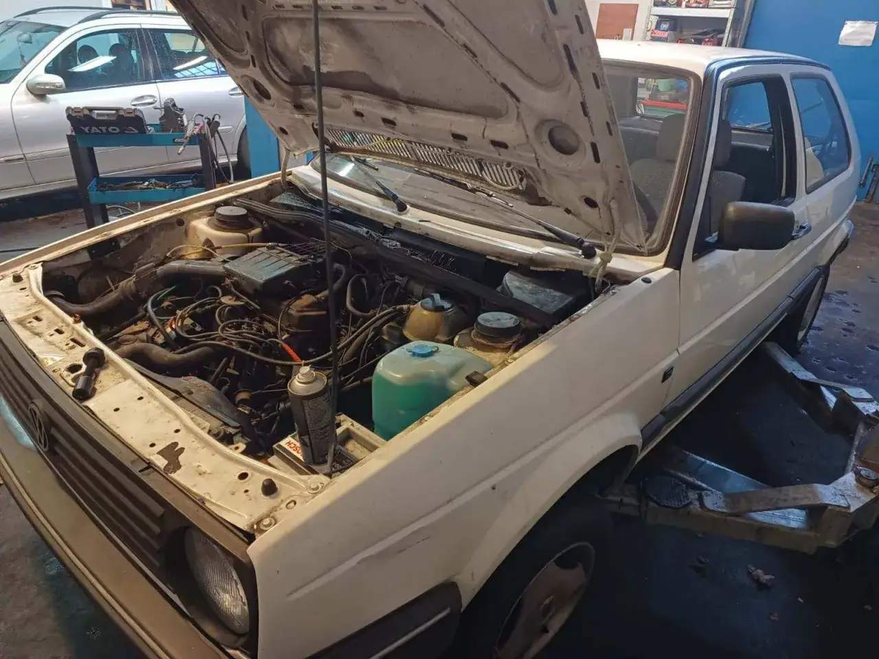 Biały Volkswagen Golf z otwartą maską, silnik gotowy do naprawy. Widać elementy układu chłodzenia i przewody. Może czas na nowe tłoki Kolbenschmidt?
