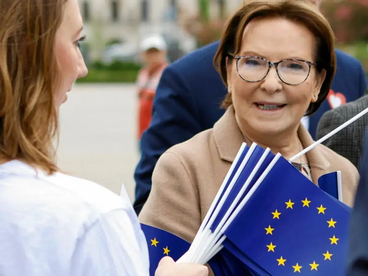 Ewa Kopacz z flagami UE, być może w miejscu, gdzie mieszka, rozmawia z młodą kobietą.