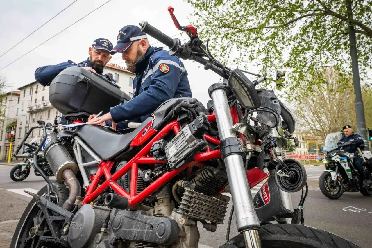 Due agenti di polizia locale controllano documenti su una moto. Sei motociclista se ti fermano per un controllo.