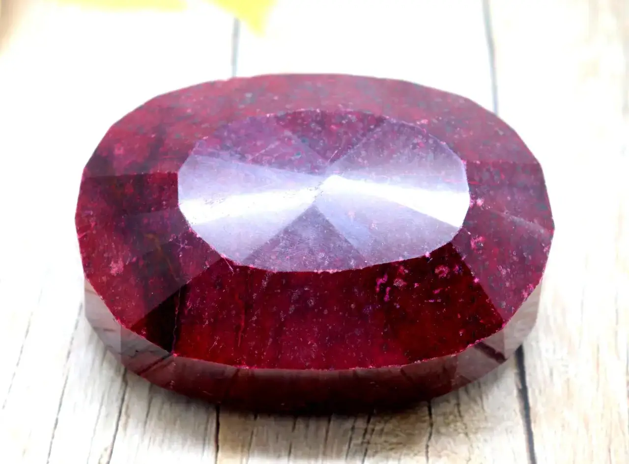 Un grande rubino sfaccettato, la pietra di luglio, brilla con inclusioni naturali su uno sfondo di legno chiaro.
