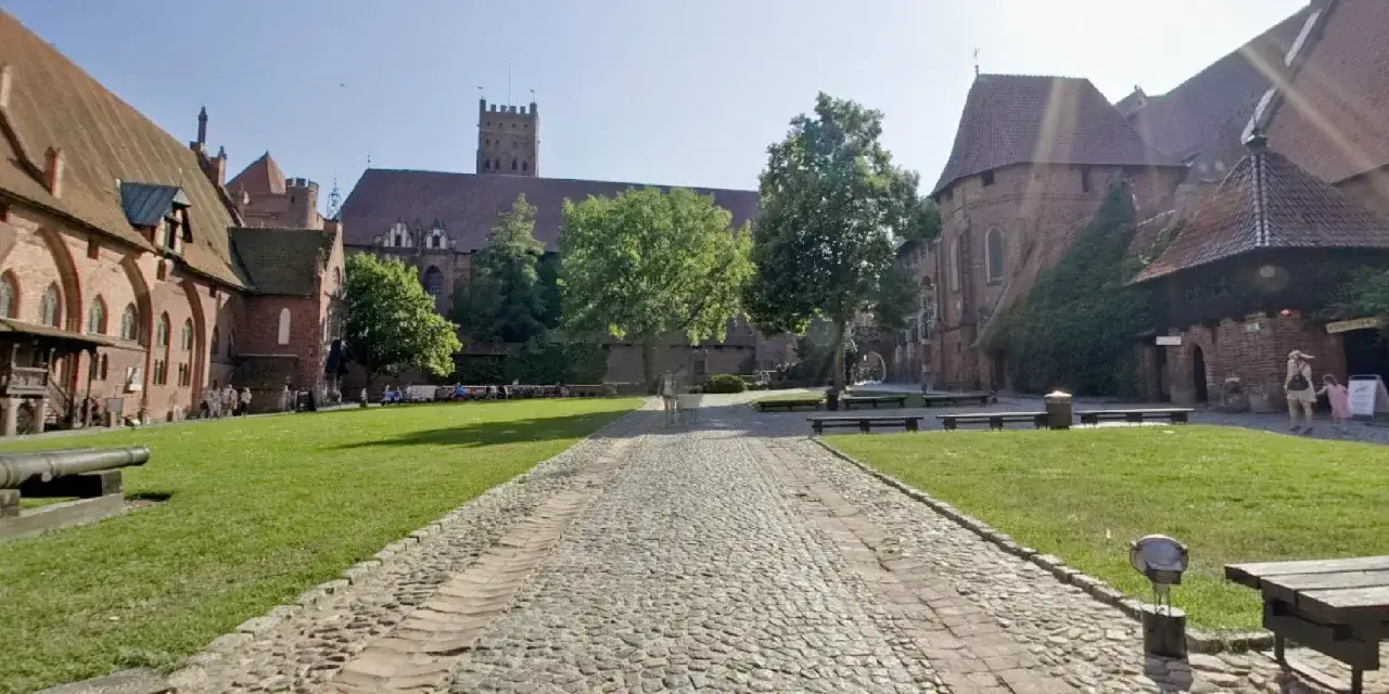 Dziedziniec zamku w Malborku, największego zamku w Polsce, z brukowaną ścieżką i zielonym trawnikiem.