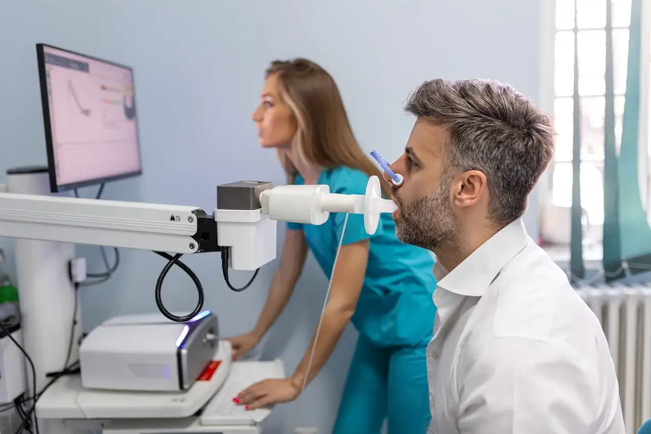 Mann macht Lungenfunktionstest mit Spirometer, w&auml;hrend &Auml;rztin die Ergebnisse auf dem Monitor beobachtet. Dies ist wichtig f&uuml;r die leitlinie asthma bronchiale.