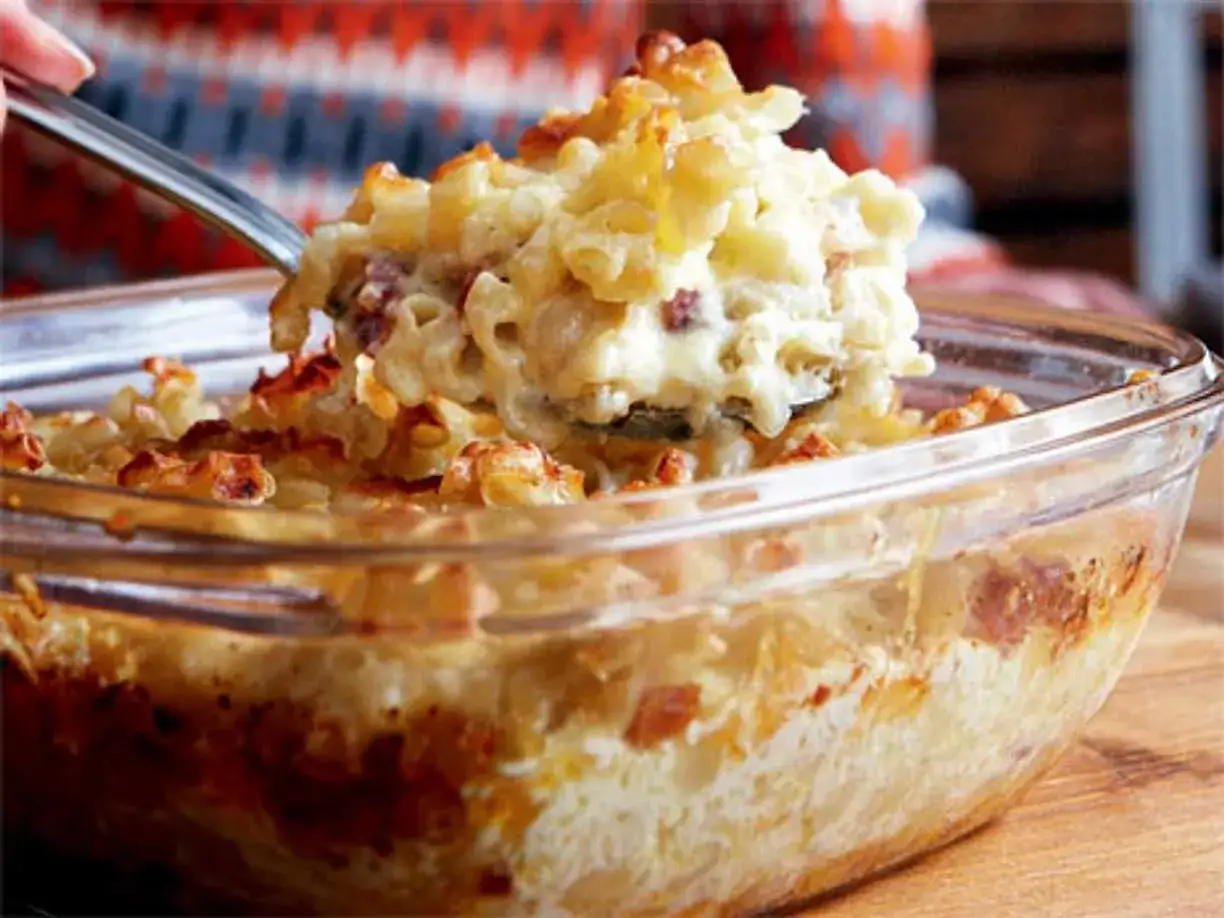 En sked lyfter upp en portion kr&auml;mig, gammaldags makaronipudding ur en glasform.