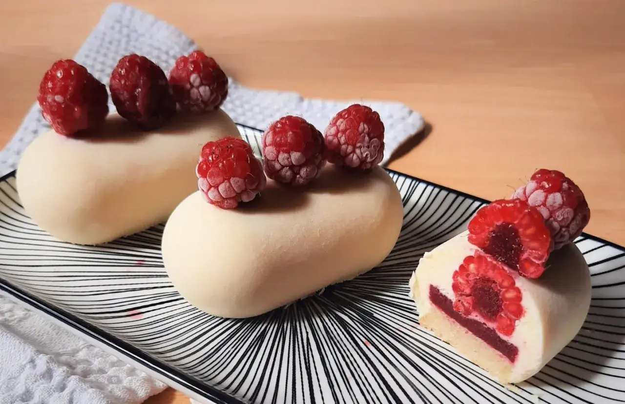 D&eacute;licieux entremet vanille, glac&eacute; et garni de framboises fra&icirc;ches, sur une assiette graphique.