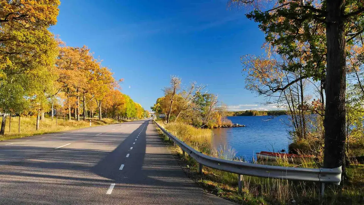 Herbstliche Allee f&uuml;hrt zu einem See. Was muss man in Schweden gesehen haben? Diese malerische Stra&szlig;e mit bunten B&auml;umen und ruhigem Wasser ist ein Muss.