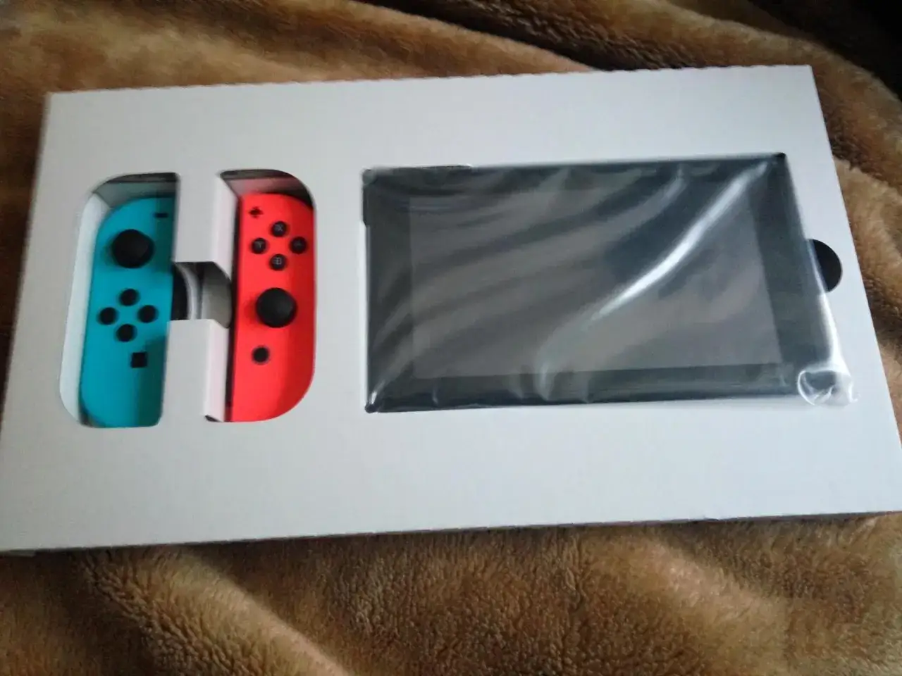 Nowa konsola Nintendo Switch w pudełku, z niebieskim i czerwonym Joy-Conem obok ekranu.