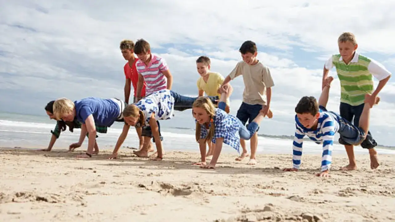 Niños jugando a la carretilla en la playa. ¡Una idea genial que hacer en vacaciones con niños para divertirse al aire libre!