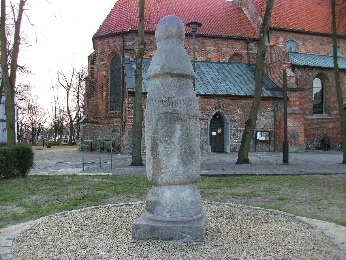 Kamienny słup milowy z inskrypcją przed ceglanym kościołem.