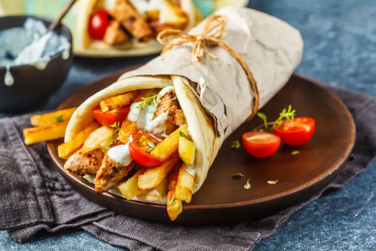 Pyszne greckie jedzenie: gyros zawinięty w placek z frytkami, pomidorkami i sosem.