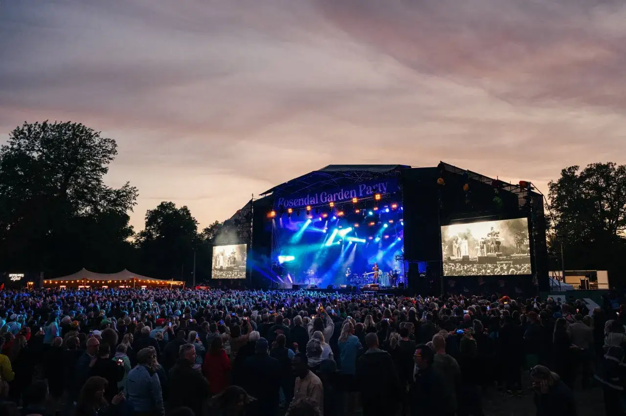 Stor publik vid Rosendal Garden Party. En stor scen med bl&aring; ljus och band. En storbildssk&auml;rm visar artisterna.