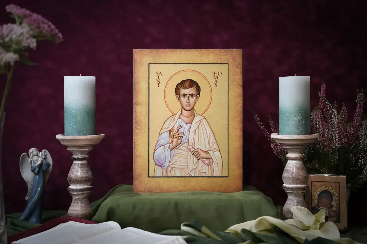 Piękny icon po polsku przedstawiający św. Tomasza z Apostołów, otoczony świecami i kwiatami.
