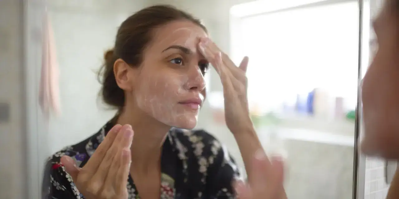 Une femme applique une mousse nettoyante sur son visage, un moment de démaquillage visage apaisant.