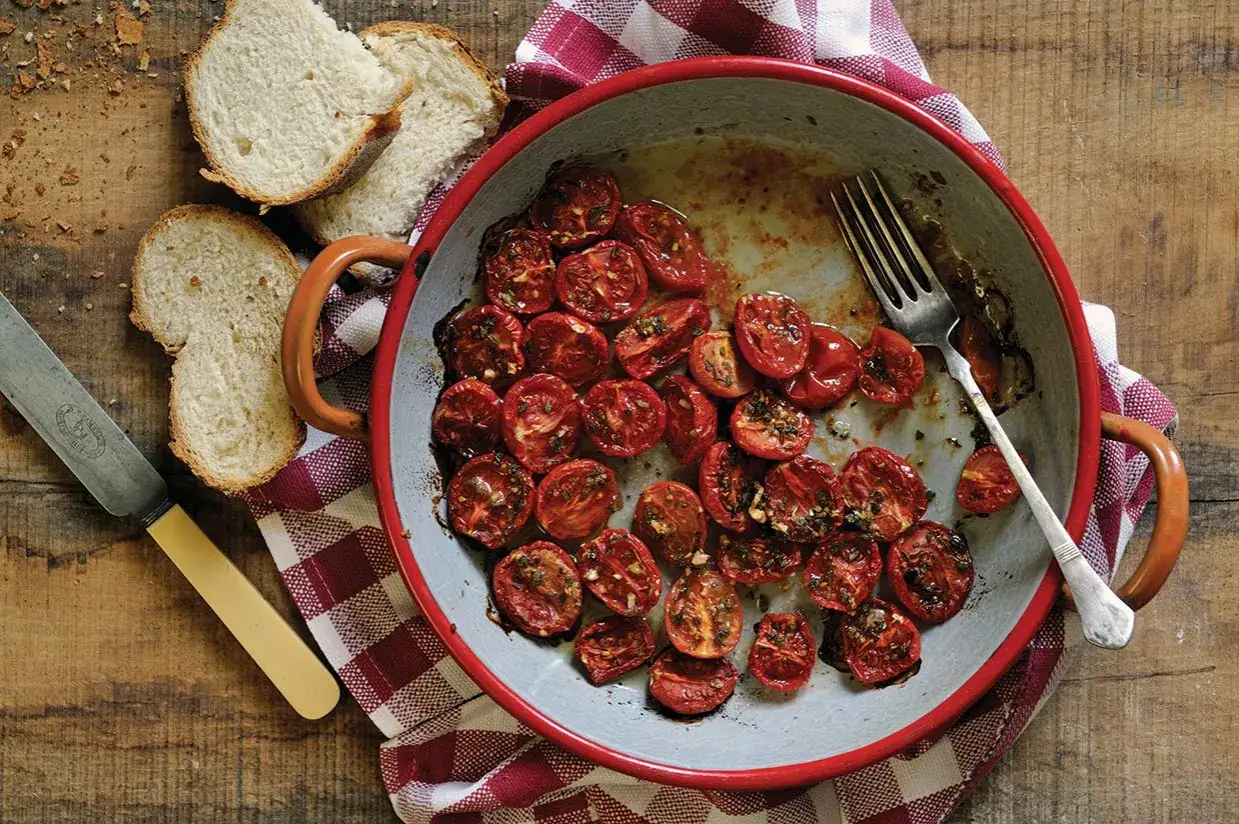 Karamellisierte Tomaten in einer Pfanne, daneben Brot und Besteck.