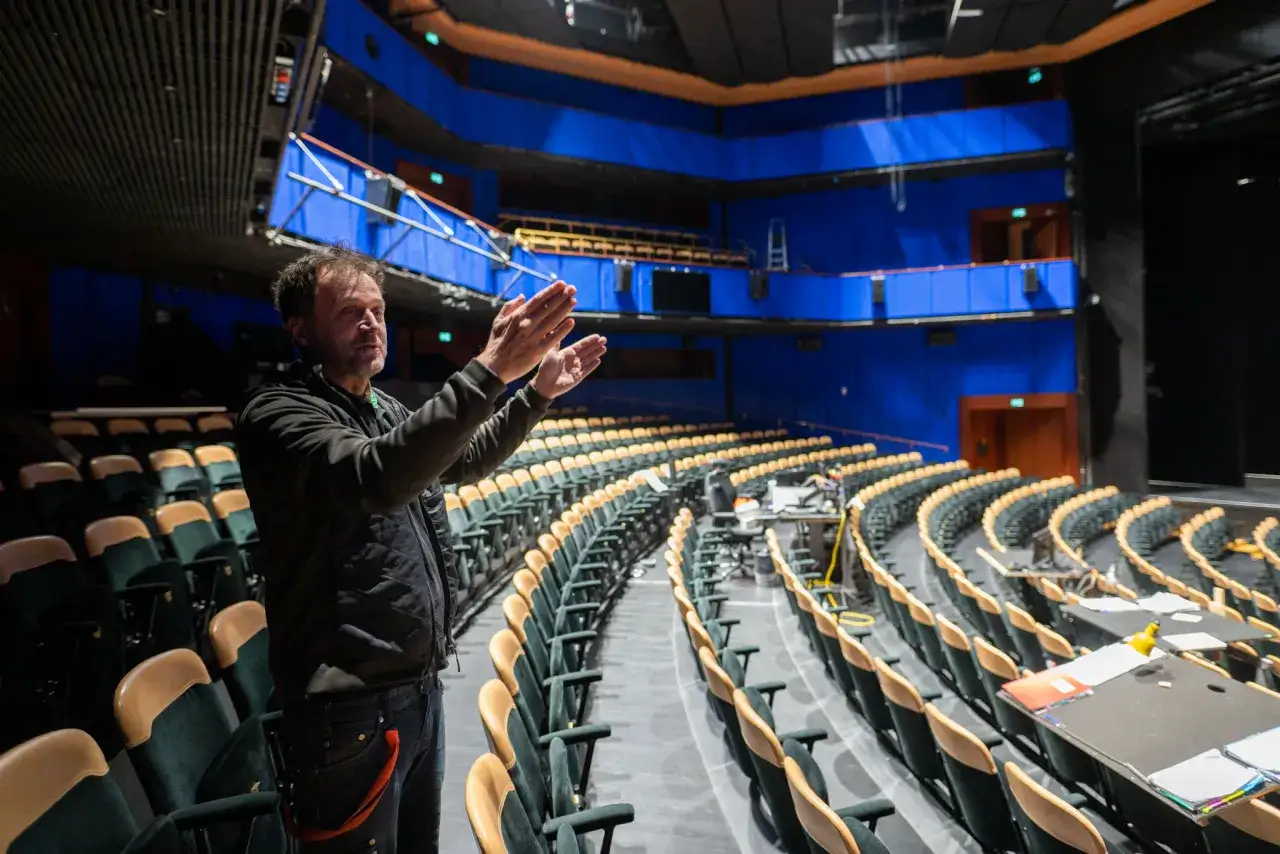 Man klappar händerna i en tom teater med blå väggar, redo för soppteatern i Stockholm.