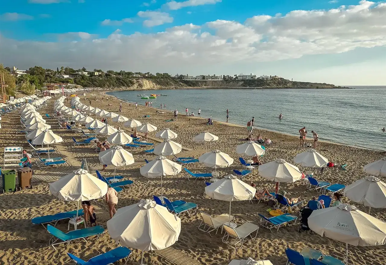 Piękna plaża na Cyprze w listopadzie. Pogoda sprzyja relaksowi pod białymi parasolami, a morze zachęca do kąpieli.