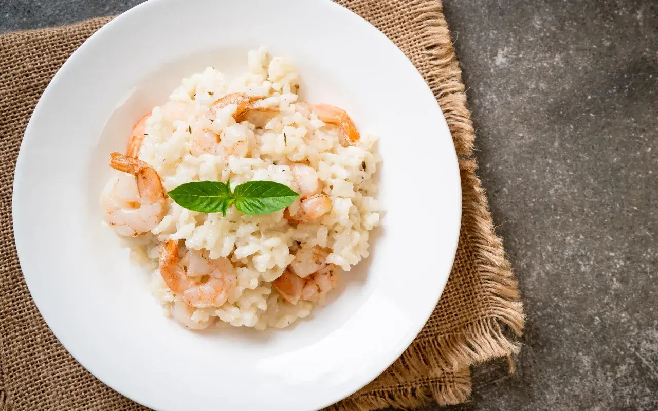 Kremowe risotto z krewetkami, udekorowane listkiem bazylii, podane na białym talerzu.