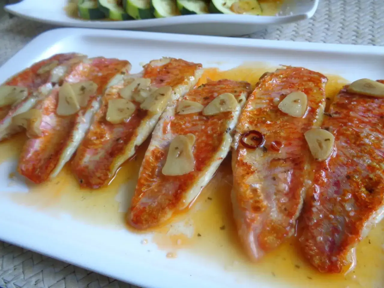 Deliciosos salmonetes a la plancha con l&aacute;minas de ajo y un toque picante, servidos en una bandeja blanca.