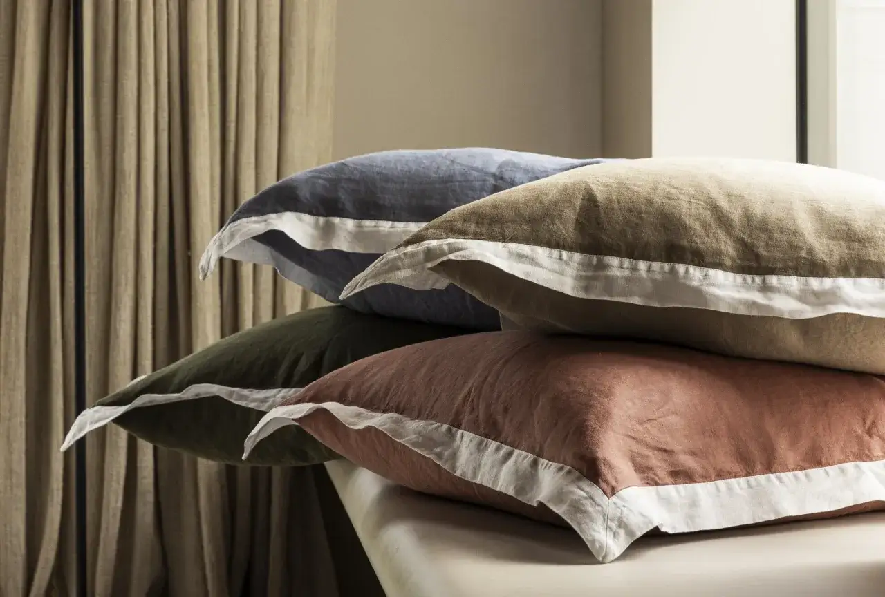 Pile de coussins aux couleurs douces, bleu, kaki, brun et rose, bordés de blanc. Le percale de coton, c'est quoi ? Une matière douce et respirante.