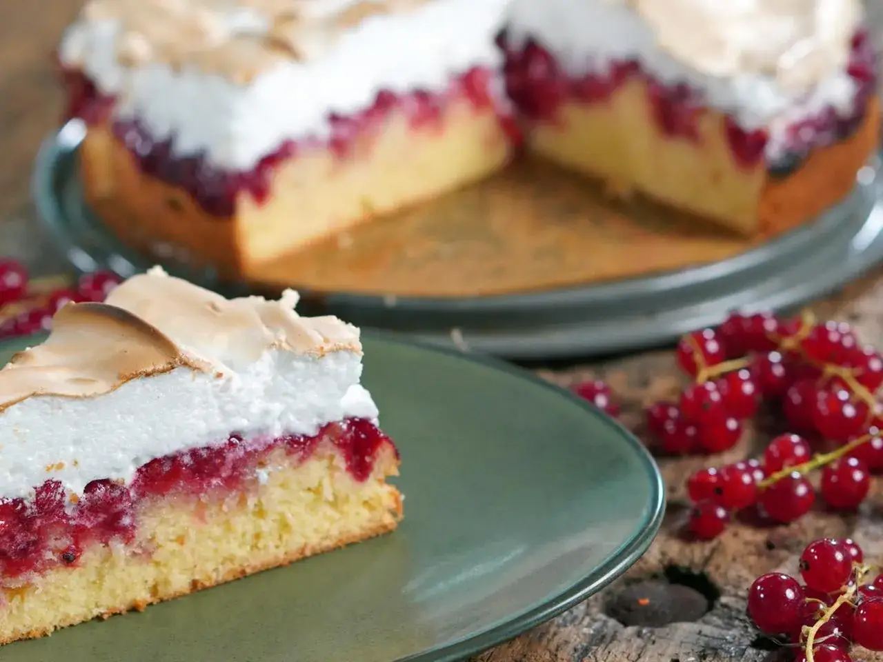 Ein Stück saftiger Johannisbeer Baiser Kuchen auf einem grünen Teller, daneben rote Johannisbeeren.