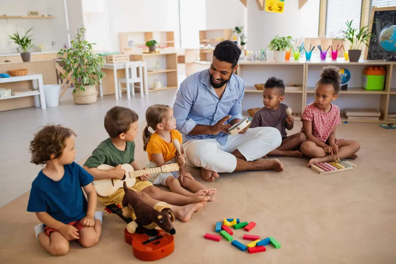 Un homme joue de la musique avec des enfants dans une classe. L'ambiance est joyeuse, une scène qui pourrait être l'équivalence BAFD d'une journée réussie.