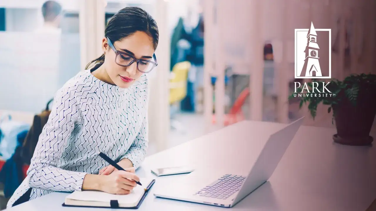 Eine Frau mit Brille schreibt Notizen, w&auml;hrend sie &uuml;berlegt, was ist Copywriting. Laptop und Handy liegen bereit.