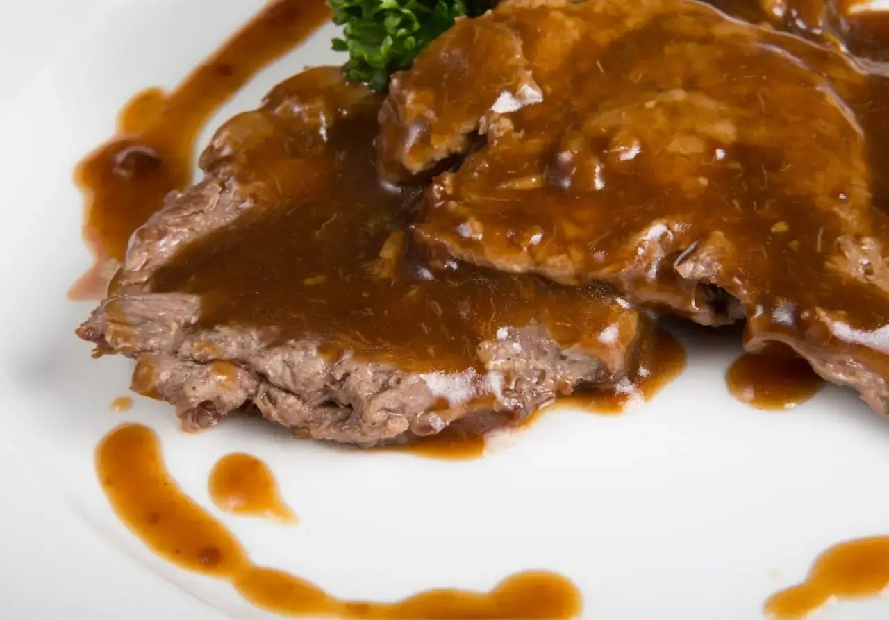 Arrosto di vitello morbido con sughetto invitante, guarnito con prezzemolo fresco.