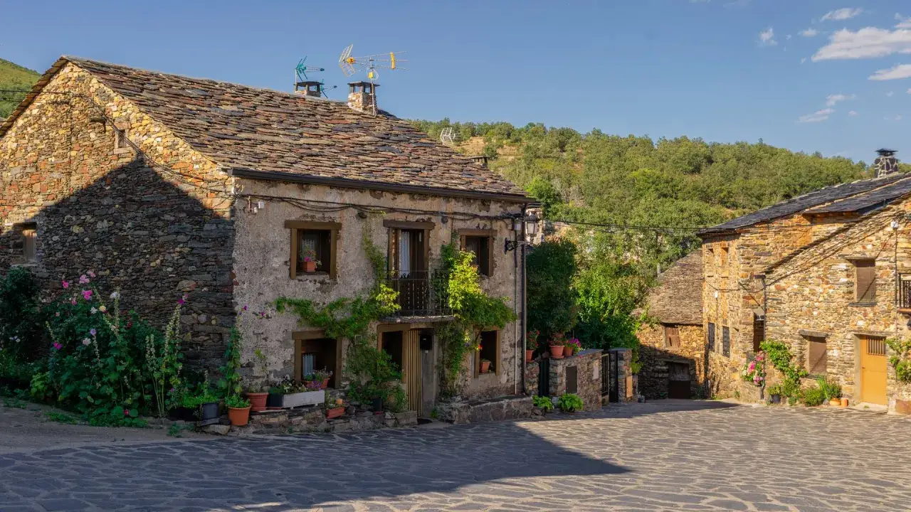 Casas de piedra con tejados de pizarra en un pueblo de la sierra de Guadalajara, con vegetaci&oacute;n y flores adornando las fachadas.