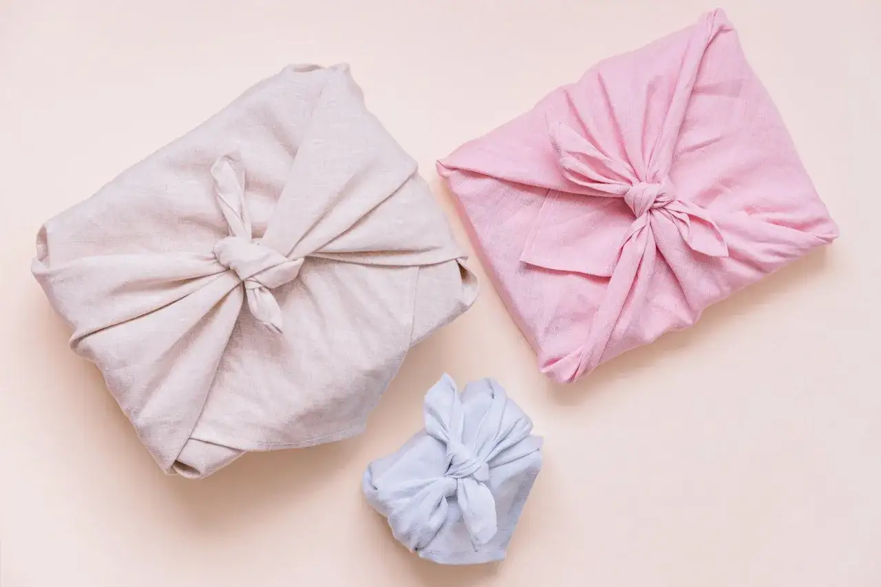 Trois cadeaux joliment emballés dans des tissus de différentes couleurs. Quel tissu pour furoshiki ? Le lin semble idéal pour un emballage élégant et écologique.