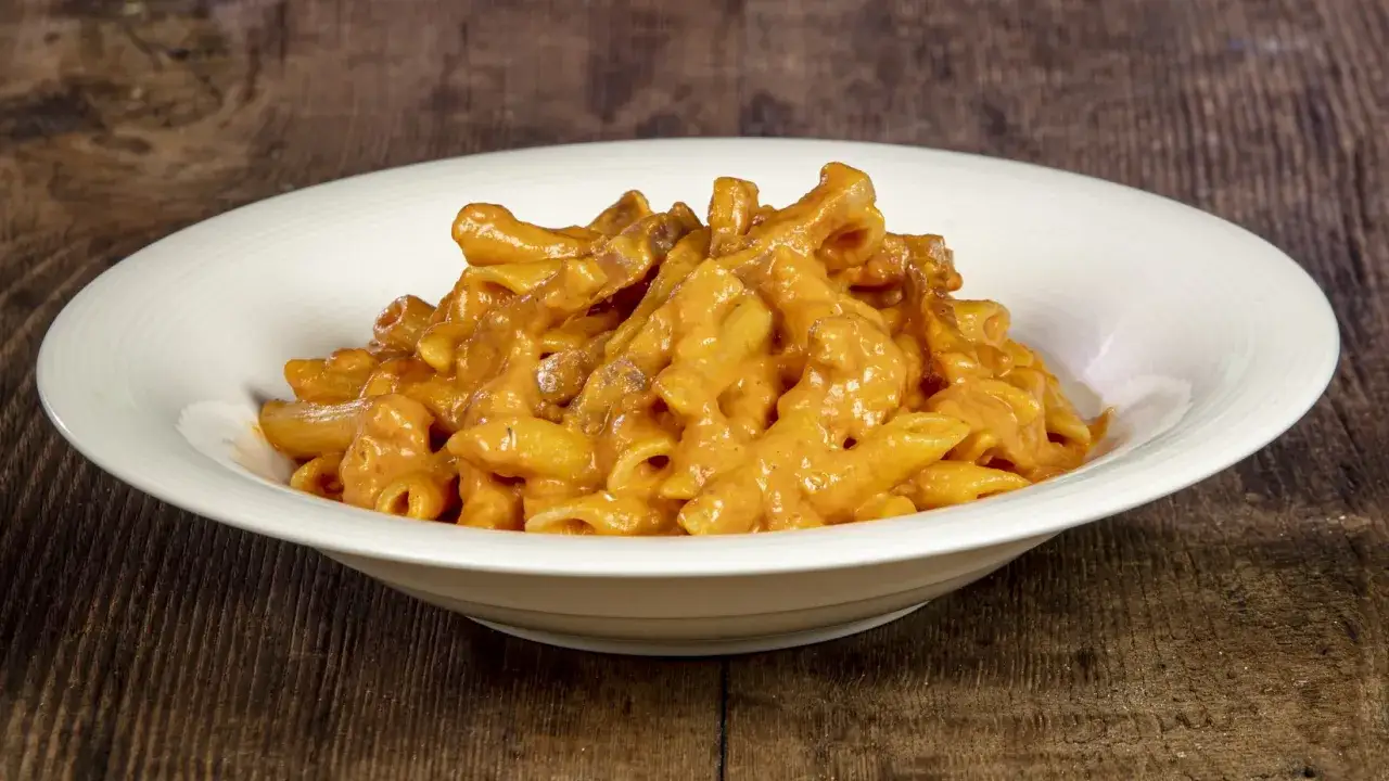 Penne alla vodka cremose e invitanti, servite in un piatto bianco su un tavolo di legno rustico.